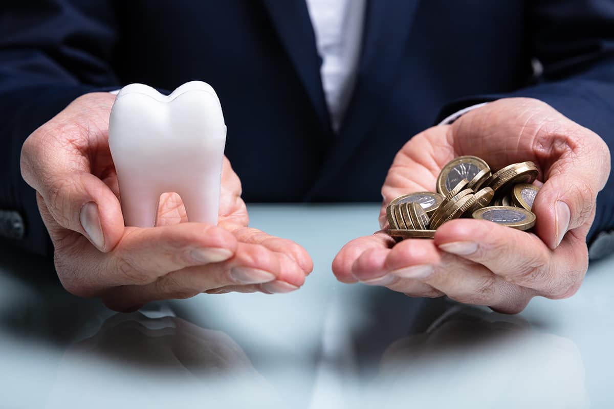 business person holding tooth and coins weighing the cost of dental implants