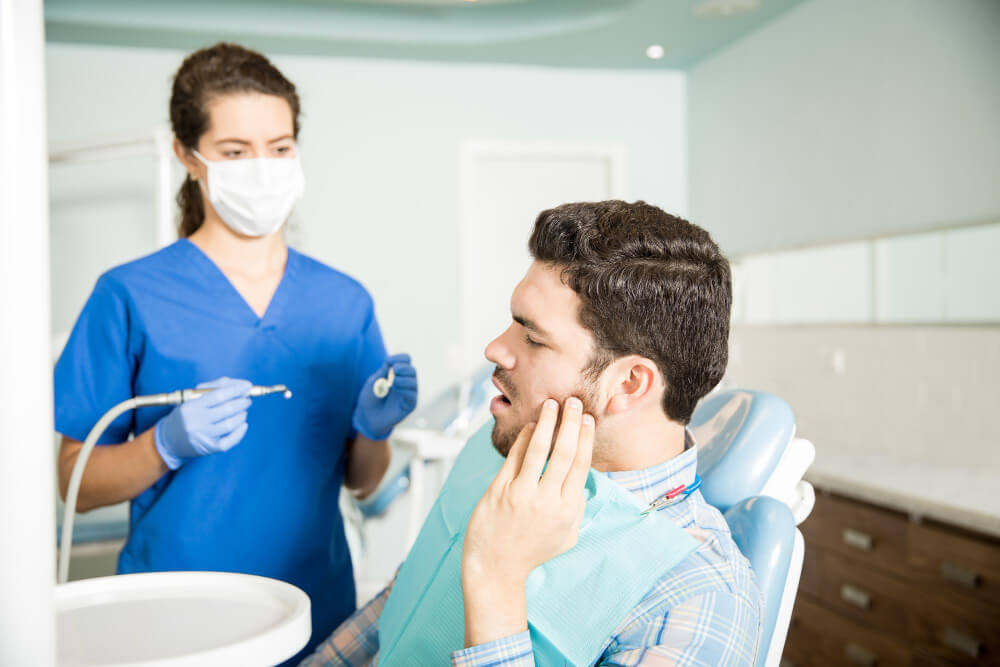 a man at the dentist touching his cheek due to tooth pain