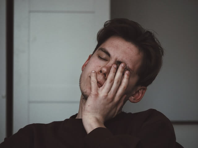 a man in black with a palm  on his face having tooth pain