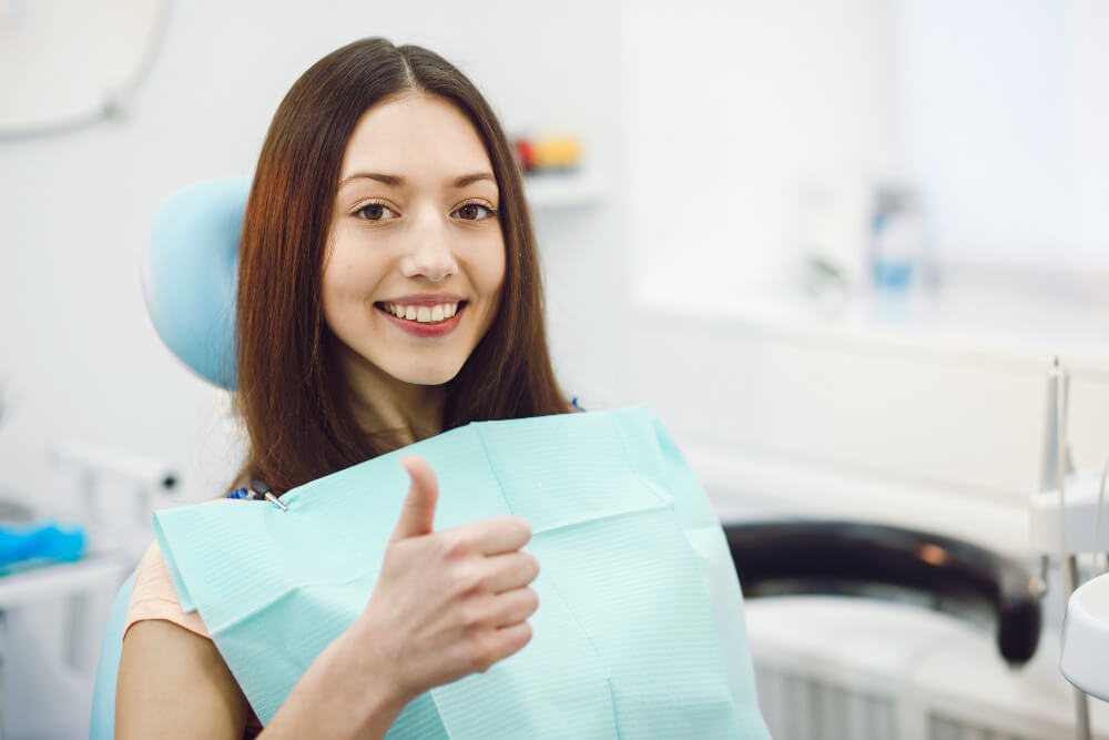 woman sitting on the dental chair, smiling while holding a thumbs up