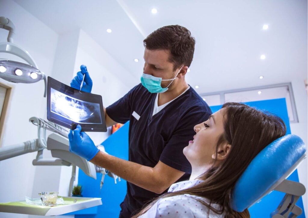 Dentist reviewing dental X-rays with a patient during a consultation, discussing the treatment timeline and healing process for a tooth implant procedure.