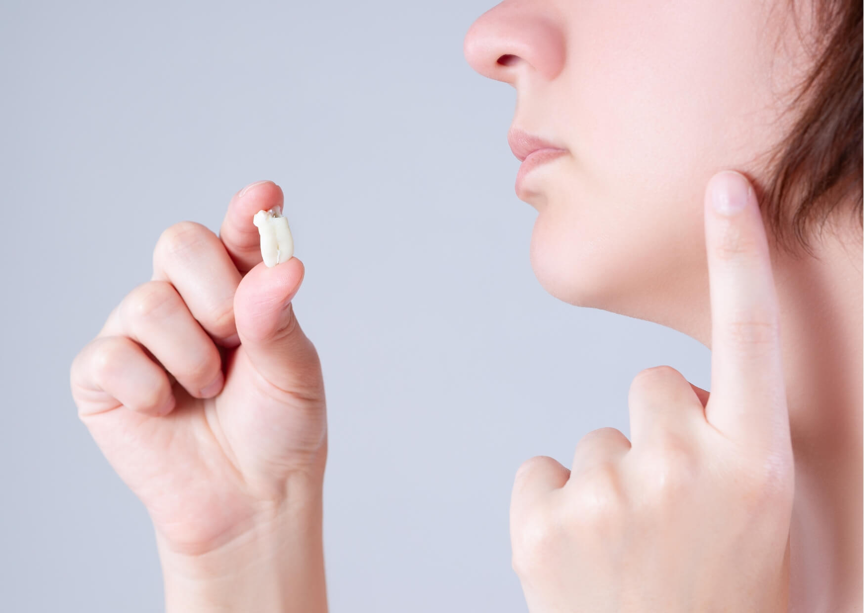Person holding an extracted wisdom tooth and pointing to the jaw area, illustrating common symptoms and timing concerns as a wisdom tooth starts to emerge.