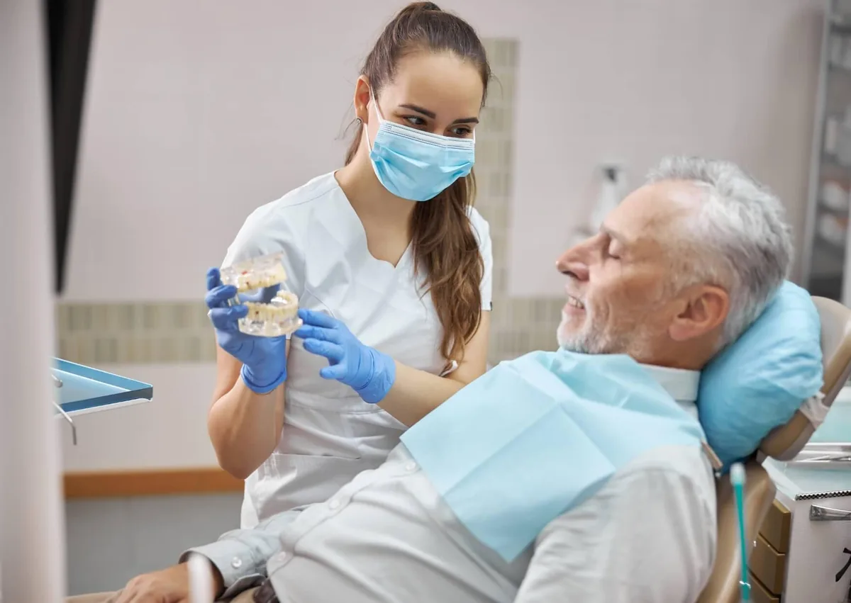 Dental professional showing an older patient a dental model while discussing affordable dental implants and tooth replacement options.
