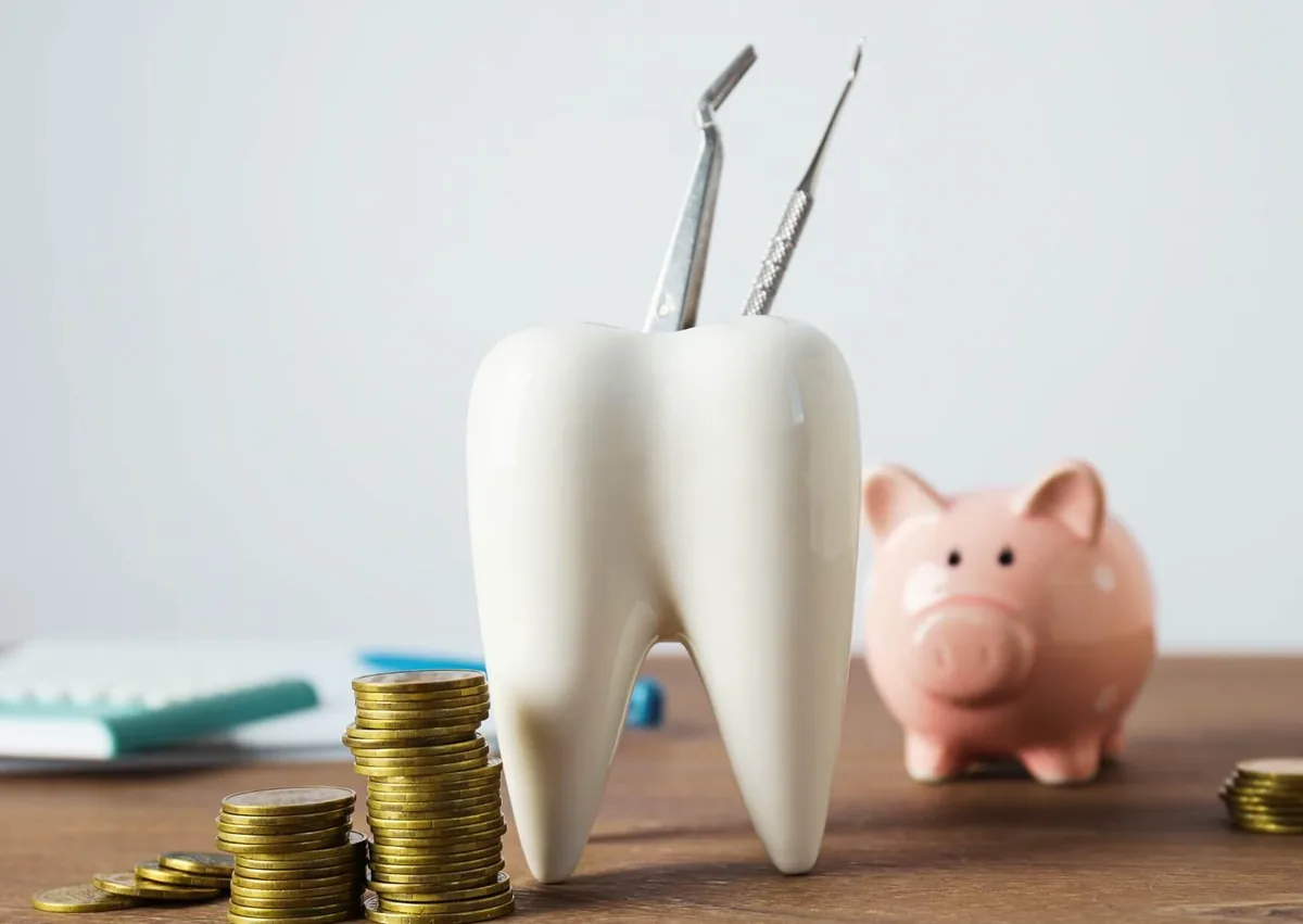 Tooth model with dental tools and coins representing the cost of dental bonding treatment.