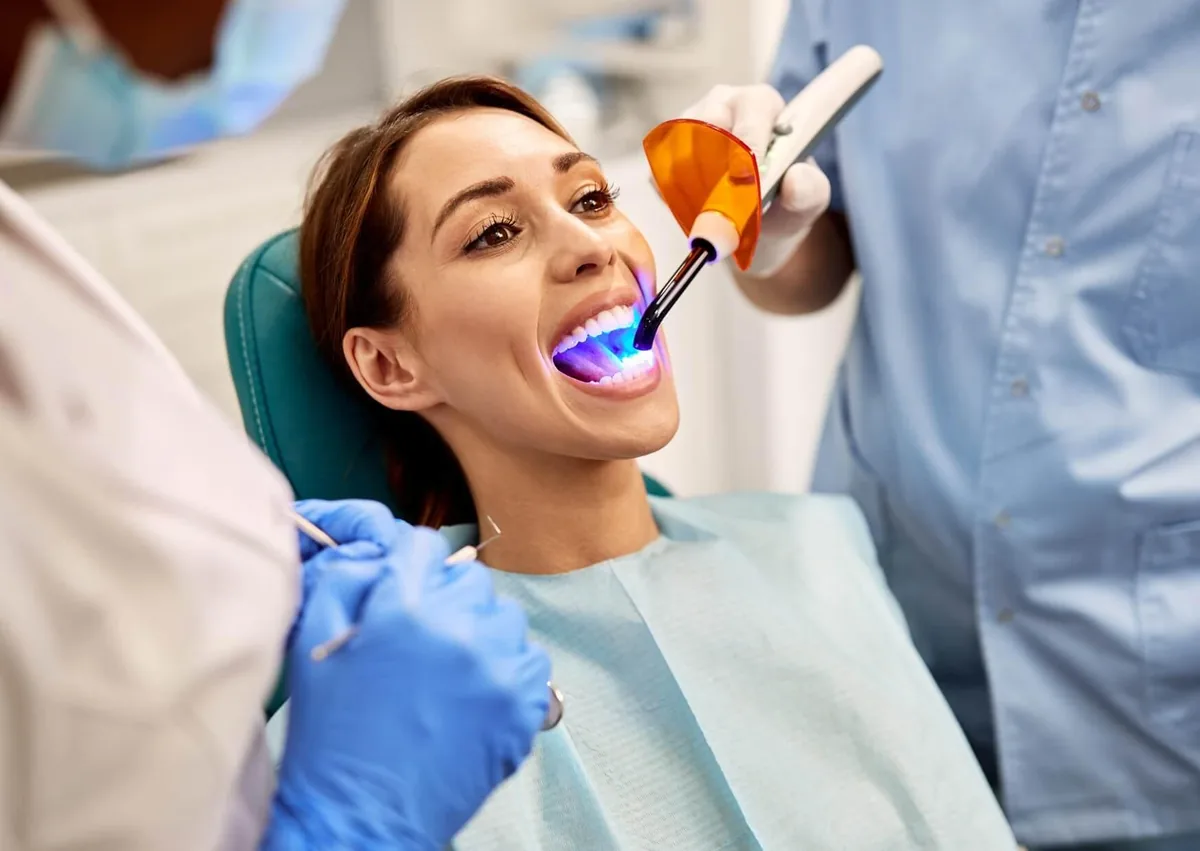 Dentist using a curing light during a dental bonding procedure on a patient’s teeth.