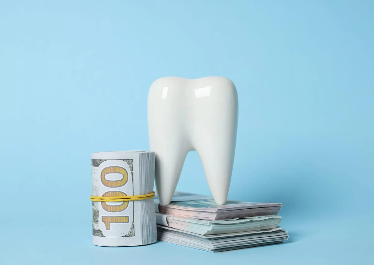 White tooth model beside stacks of money, representing teeth bonding costs and affordable cosmetic dental treatment options.