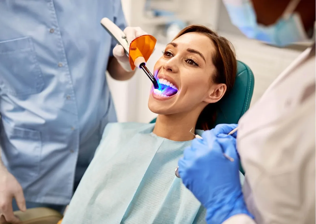 Dentist using a curing light on a patient's teeth during a cosmetic dental bonding procedure to harden tooth-colored composite resin.