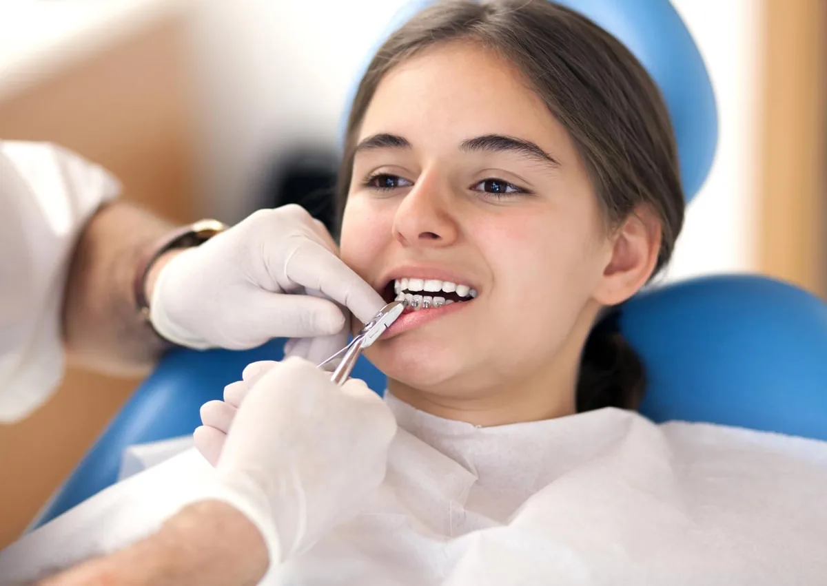 Orthodontist adjusting metal braces on a young patient's teeth during an appointment, illustrating treatment involved in the overall cost of braces.